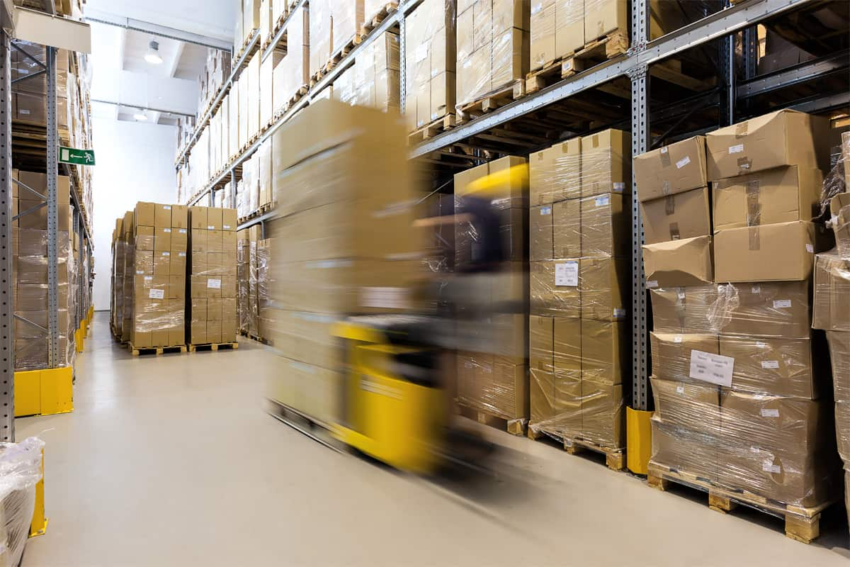 3PL warehouse filled with stacked boxes on shelves, warehouse employee moving inventory